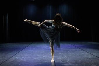 A student dancer balances on one leg on a stage.